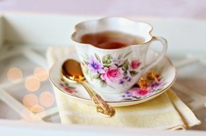 a flowered tea cup with tea in it, a golden spoon, and an impression of a fancy or high tea