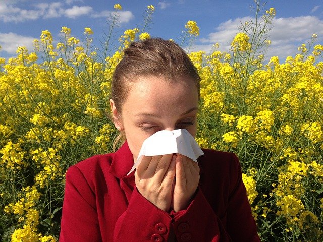 woman sneezing into a tissue in front of flowers