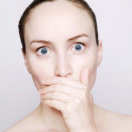 naked woman from the clavicle up covering her mouth with her hand